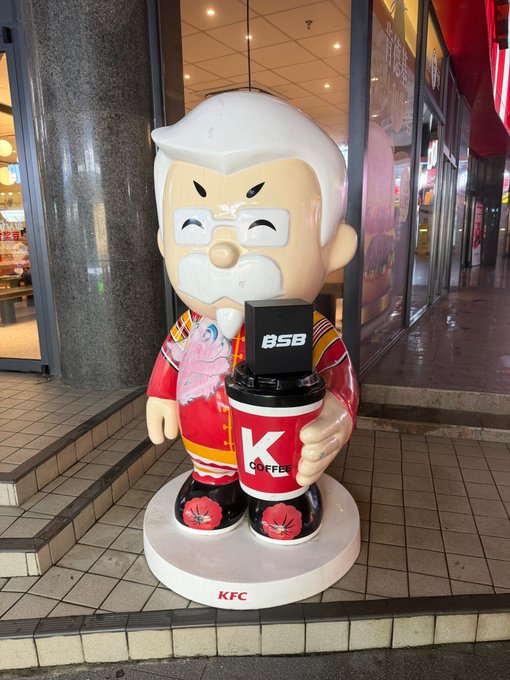 A life-sized statue of Colonel Sanders stands outside a KFC, dressed in traditional Chinese attire and holding a cup of K Coffee alongside a "BSB" crypto ATM, visually merging fast food branding with cryptocurrency adoption. The base displays "KFC," while the ATM screen shows "BSB," directly illustrating the post's clever menu pun of "KFC with a side of 30TH/s BSB."