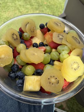 A clear bowl is filled with assorted fresh fruit, including grapes, blueberries, strawberries, kiwi, pineapple, and melon.