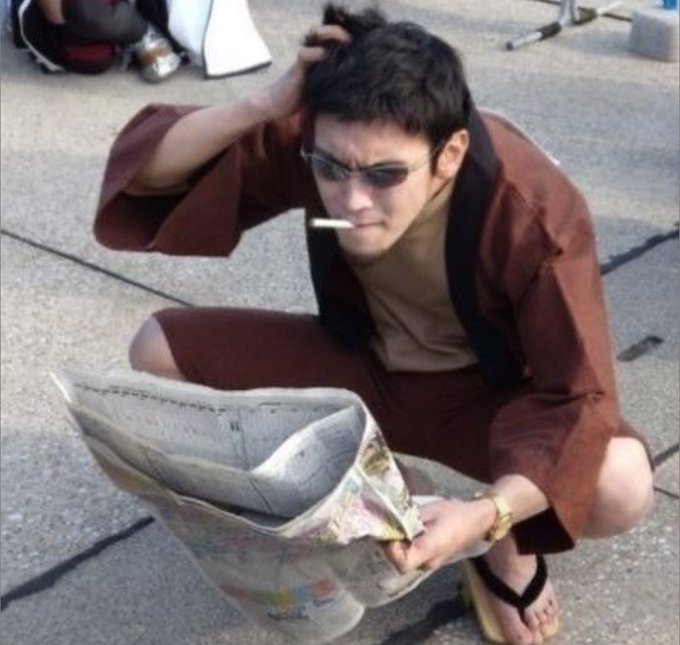 A man wearing sunglasses and a brown robe squats on pavement, smoking a cigarette and reading a newspaper, in what appears to be a meme image.
