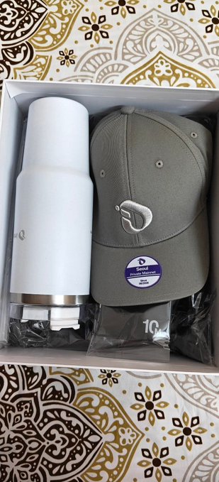 An open gift box containing a white insulated tumbler and a grey baseball cap with a 'D' logo, both bearing 'Dinamo Minsk Premium' labels, resting on a patterned fabric surface.