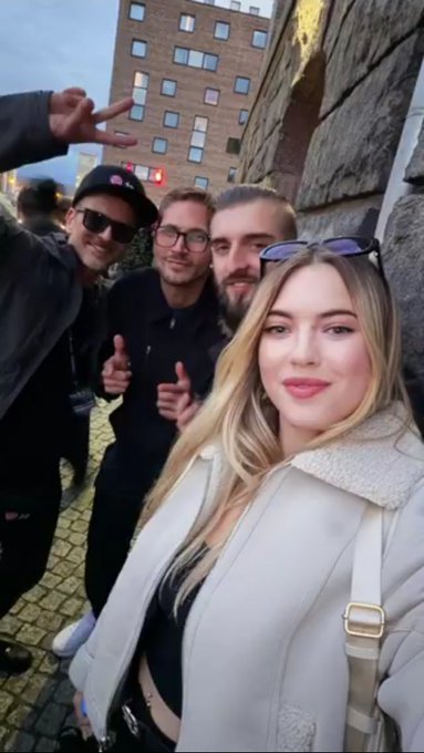 The image features a group of four people posing for a photo, with two men wearing sunglasses and one woman wearing a white jacket. They are standing next to each other against a brick wall backdrop, which suggests that they might be at an event or gathering. The caption "Take us back to Solana Summit Germany" implies that the image is related to a past event or location where they attended a summit together.