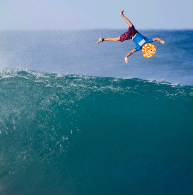 An action shot of a person in red plaid shorts doing a backflip over an ocean wave, with their face obscured by a fried egg emoji sticker.