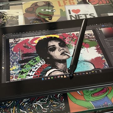A black drawing tablet displays a digital graffiti-style portrait of a woman smoking a cigarette, with a black stylus pen resting on the screen, and colorful art prints visible in the background.