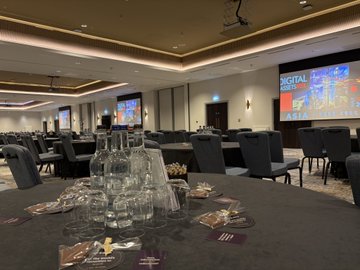 An elegant banquet hall set up with tables, chairs, glassware, and wine glasses, with a large "DIGITAL MARKETING" screen visible in the background.