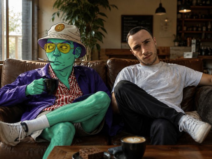 Two friends lounge on a brown leather couch in a cozy cafe, one depicted as a green-skinned character with a "B" logo hat and yellow glasses holding a mug, alongside a casually dressed man — fitting the "gm everyone" vibe as Bitcoin pumps and they discuss which crypto to buy next.