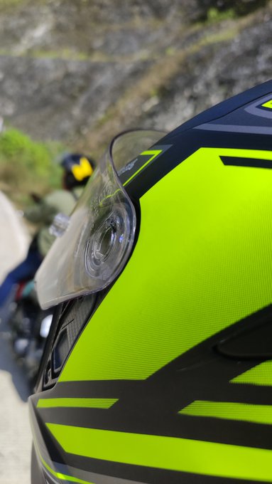 A close-up view shows a neon yellow and black motorcycle helmet with a clear visor, with a rider visible in the background.