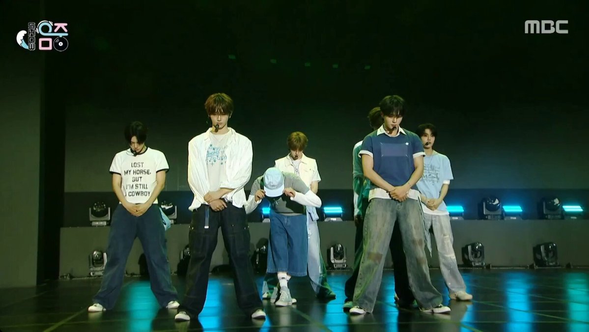 The image features five young men dressed in matching outfits, standing together on a stage with their arms crossed. They are all wearing white shirts and blue jeans, creating a sense of unity among them. The background shows a dark room with multiple lights, which further emphasizes the group's presence on stage. The caption "260620_Ulmufe OMG #ALPHADRIVEONE #ALD1 #ALPHADRIVEONE" suggests that this image is related to a post or social media content featuring these young men and their performance.