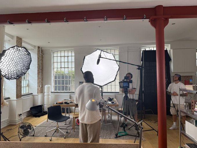 Behind-the-scenes photo of a video or photo production setup with lighting equipment, cameras, and crew members in a studio space.
