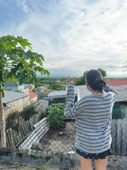 A person in a striped hoodie stands with their back to the camera, taking in a scenic view of rooftops and distant mountains under a partly cloudy sky.
