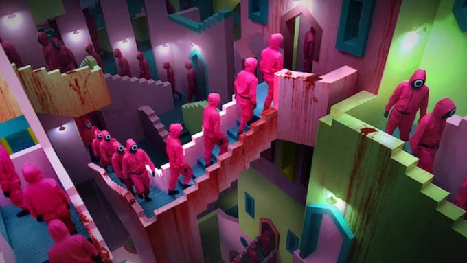 ersatz characters in pink suits walk on a pink bridge, with a green building and white walls in the background.