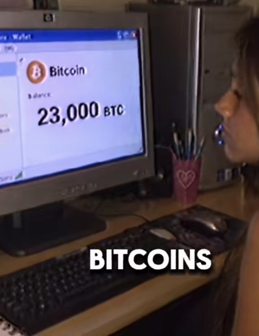 A young girl looks at a computer monitor displaying a Bitcoin wallet balance of 23,000 BTC, with the word "BITCOINS" overlaid on the screen.