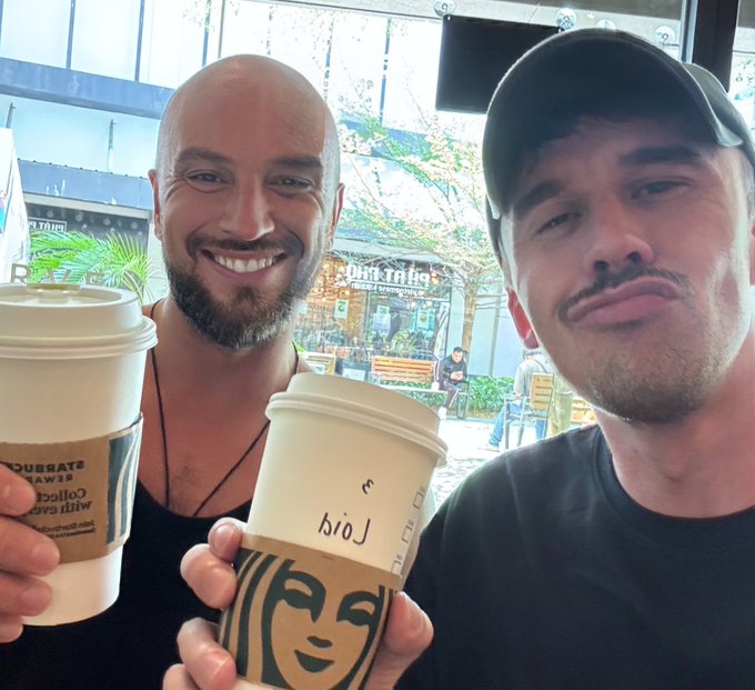 The image features two men holding coffee cups, with one of them smiling at the camera while the other looks away from the camera. The background includes a window that offers a view of trees outside. The caption for the image reads "gm web4 @NomadicSesh just joined in Philippines for some new adventures! Let’s build the agentic future together".