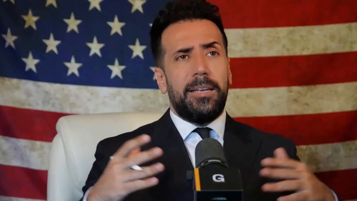 The image features a man wearing a suit, seated behind a microphone with his hands outstretched as if he's giving a speech or interview. The backdrop of the scene is an American flag, which adds a patriotic touch to the setting. The caption "Big Facts @x" suggests that there might be some information or data being discussed in this image.