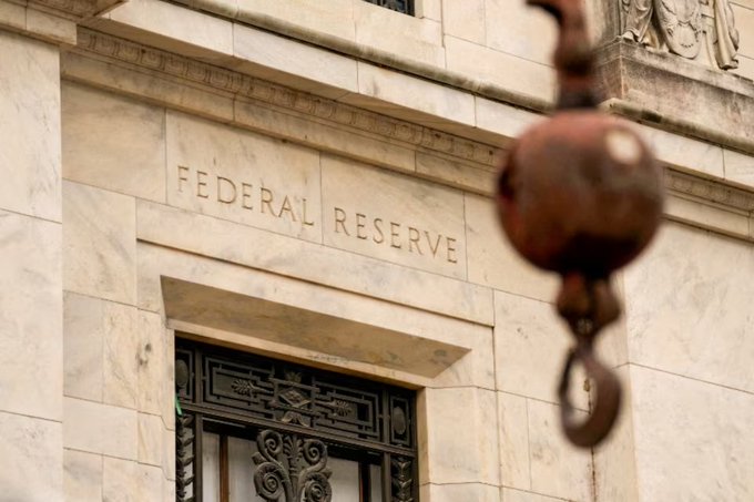 A close-up architectural shot of the "FEDERAL RESERVE" building entrance with an ornate door and a decorative metal fixture in the foreground.