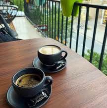 The image features a wooden table with two cups of coffee sitting on saucers. The background shows a balcony, providing an outdoor setting for enjoying a cup of coffee. A caption below the photo reads "GM 𝕏 Family! red market isn't forever, but good opportunities are usually found on days like this $SCBK @saucebook".