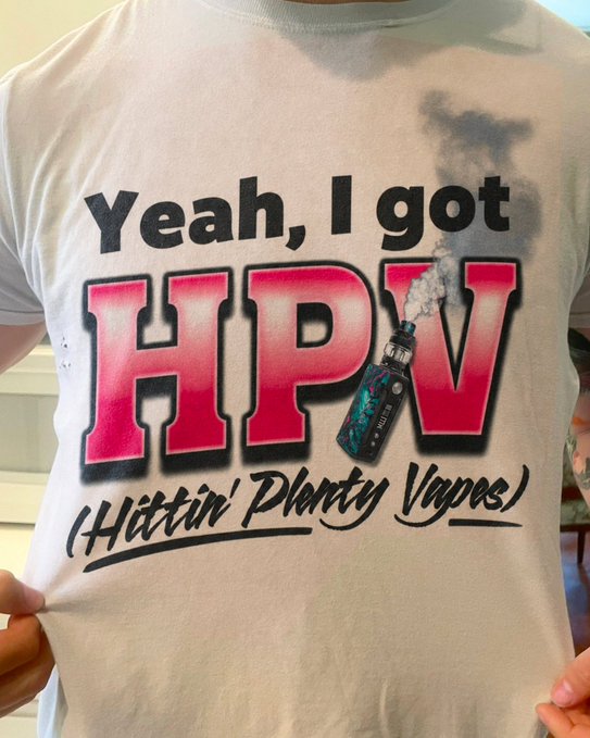 A white t-shirt with the printed text 'Yeah, I got HPV (Hittin' Plenty Vapes)' featuring pink and black letters and a vape graphic, held up by someone.