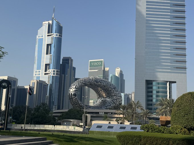 The photo shows the iconic "Museum of the Future" sculpture with Arabic calligraphy and the "VOCO" hotel sign visible, set against Dubai's skyline. The image depicts the modern Dubai Mall area where the person plans to walk laps around the city to show strength and solidarity while wearing their Zcash-branded outfit.