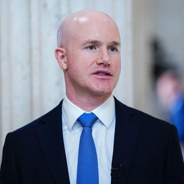 A bald man in a dark suit and blue tie, identified by context as Coinbase CEO Brian Armstrong, is shown speaking in what appears to be a formal government building setting, accompanying his public call for the CLARITY Act and his statement that "Economic security is national security."