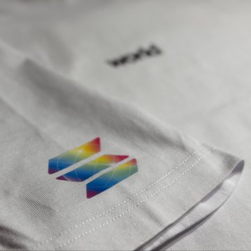 A close-up of a white fabric garment featuring a colorful, geometric rainbow-gradient logo embroidered near the bottom edge.