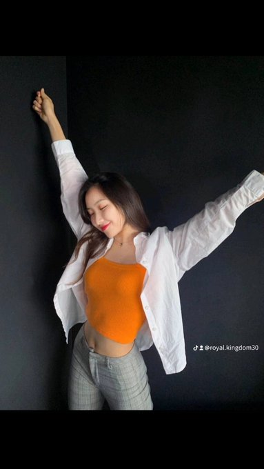 A young woman in an orange crop top and white jacket dances against a dark wall with her arms raised, with the TikTok handle @royal.kingdom30 visible.
