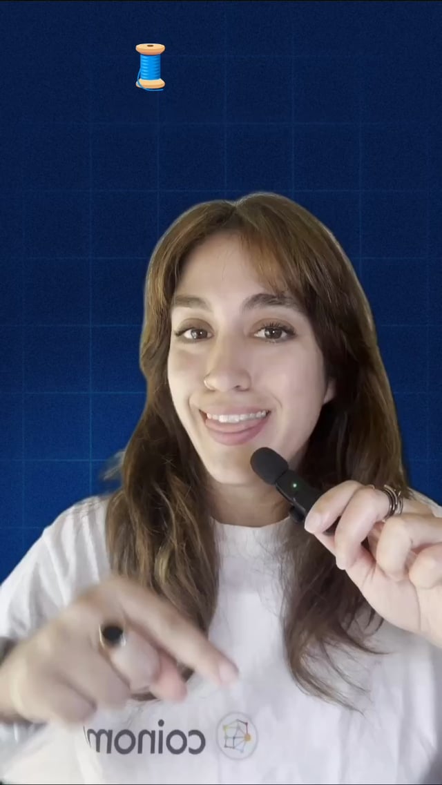 The image features a woman wearing a white shirt, holding a black microphone up to her face as if she's recording herself or giving a speech. The background of the photo has a blue grid pattern, which adds an interesting visual element to the scene. There is also a small spool of thread visible in the top left corner of the image.