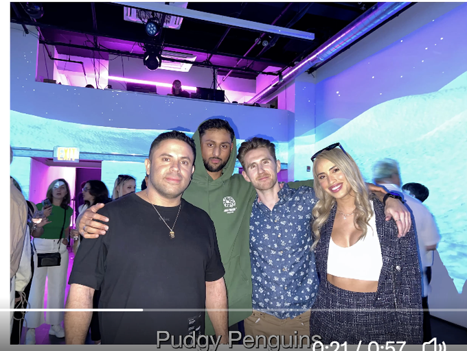 Four people pose together for a photo in a modern venue with blue ambient lighting and purple ceiling lights, with the text 'Puddy Penguins' visible at the bottom.