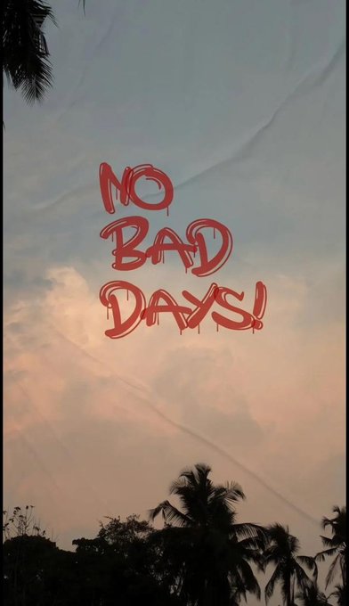 The image features a poster with the phrase "No Bad Days!" written in red letters against a blue sky backdrop featuring clouds, palm trees, and other natural elements. The text appears to be graffiti or street art, adding an urban touch to the scene. The poster is displayed on a gray wall, which contrasts with the vibrant colors of the message.