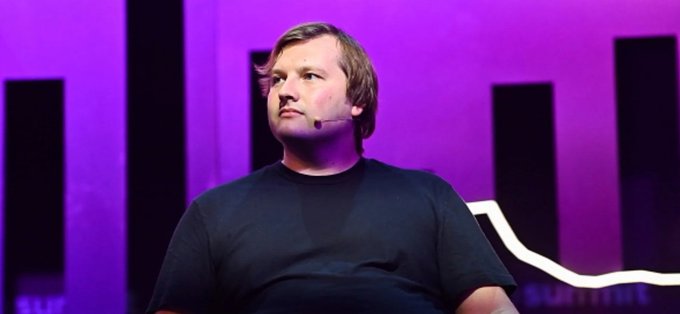 A man, likely Stani Kulechov, stands on stage wearing a black shirt and headset microphone against a purple-lit backdrop with "SU" and "SUMMIT" text visible. The image accompanies a post about his controversial proposal suggesting DeFi should adopt Uber's "move fast" regulatory approach following the Senate's rejection of the Clarity Act.