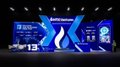 A vibrant blue-lit HTX Ventures booth at TOKEN2049 Singapore features a large "X" logo with "#13" displayed on a screen, where attendees gathered for futuristic-themed games, giveaways, and a special appearance by Justin Sun.