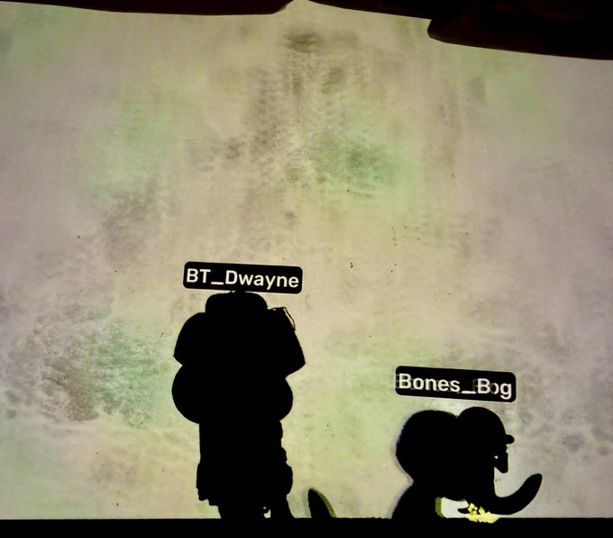 A shadow puppet performance or shadow box scene showing two silhouettes labeled 'BT_Dwayne' and 'Bones_B)g' against a mottled background.