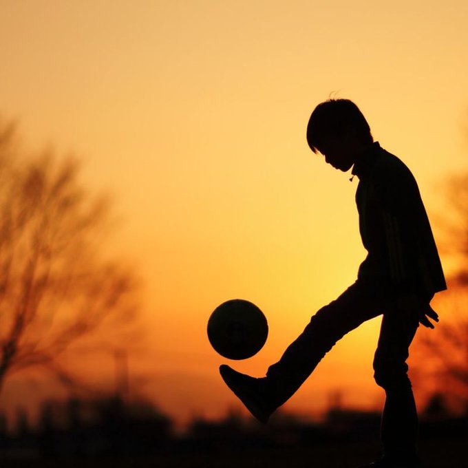 A silhouetted young boy skillfully juggles a soccer ball against a warm orange sunset, perfectly capturing the spirit of the caption "Gm practice make legends" as he dedicates himself to his craft in pursuit of greatness.