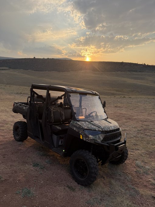 A camouflage-patterned utility terrain vehicle (UTV) parked in a field at sunset.
