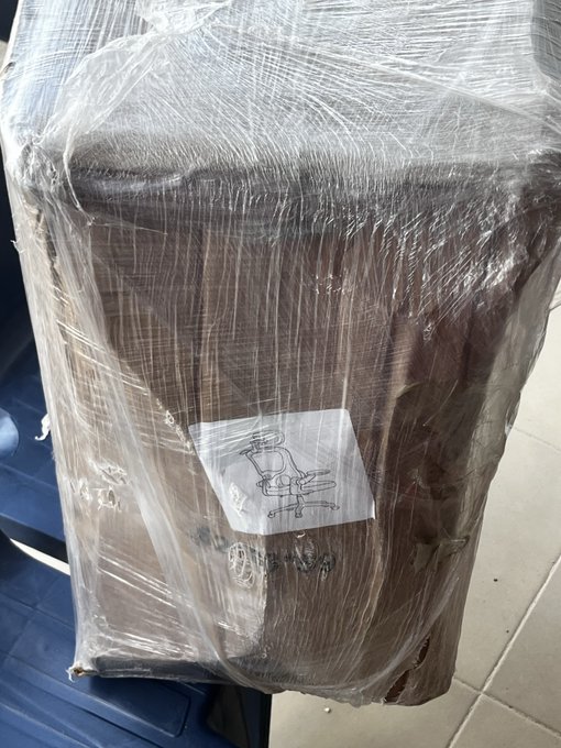 A large brown armchair wrapped in clear plastic with a white label showing a chair diagram attached to it.