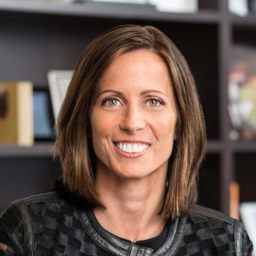 A professional woman with a warm smile, wearing a dark patterned jacket, is photographed in what appears to be an office or library setting with shelving visible behind her. The image accompanies a quote from Nasdaq CEO Adena Friedman discussing how tokenizing financial assets like equities and Treasurys could unlock tens of billions in collateral currently tied up across global finance.