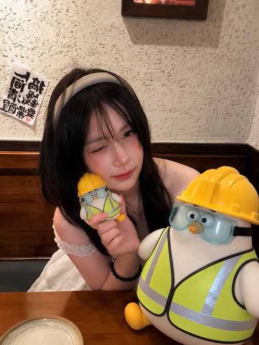 The image features a woman wearing a hard hat, holding an ice cream cone, and posing with two toy penguins - one yellow and one white. The scene takes place at a dining table or countertop where she is sitting down. There are also some Chinese characters visible in the image, which could be part of the post's title or description.