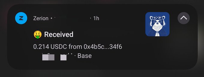 A mobile notification from Zerion showing a received transaction of 0.214 USDC from address 0x4b5c...34f6 on the Base network, with a raccoon avatar.