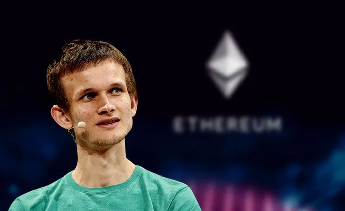 The image features a man wearing a green shirt who appears to be looking up at something, possibly an audience member or speaker. The background of the image shows a large white "Ethereum" logo with the word "EF" written on it. There is also a blurred crowd in the background, suggesting that this event might be taking place at a convention or gathering related to Ethereum technology and blockchain.