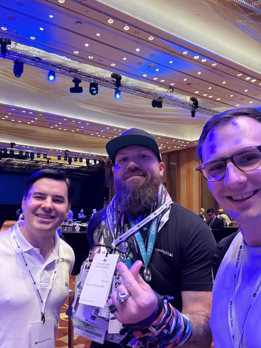 A bearded man wearing a Ruby on Rails conference ("RubyConf") badge poses with two younger men, with the text "PicoWizard" visible on his lanyard, suggesting he is a prominent figure in the Ruby on Rails community who also advocates for PicoWizard at crypto events.