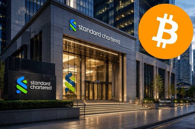 The image shows a Standard Chartered bank building with the bank's logo prominently displayed on the exterior, alongside a large orange Bitcoin symbol overlaid in the upper right corner. This visual ties directly to the news that Standard Chartered has become the first international bank in the UAE to offer Bitcoin trading through eligible clients' bank accounts, with the bank's branding paired with the Bitcoin icon symbolizing this new crypto trading service.