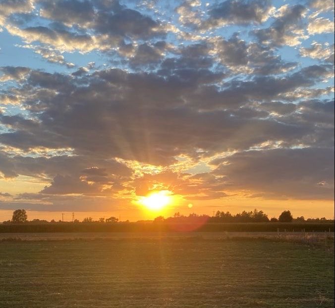 A scenic landscape photograph capturing a golden sunset with sun rays piercing through dramatic clouds over a vast open field.