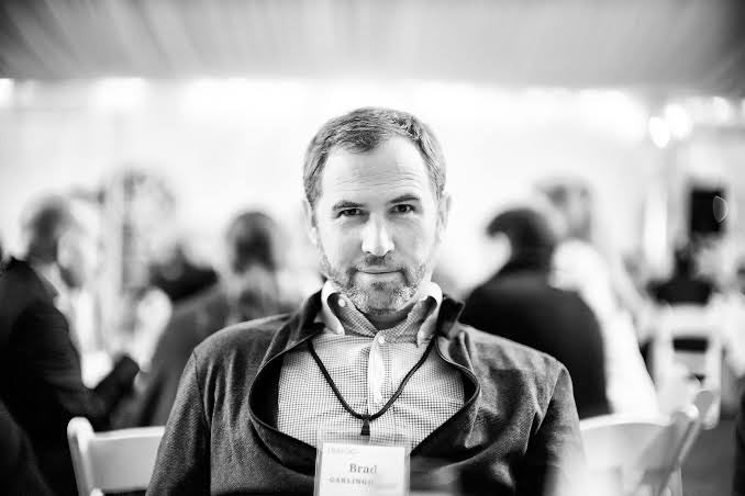 A black and white portrait of a bearded man wearing a name badge that reads 'Brad CARLING' at what appears to be a conference or event.