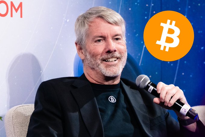 Michael Saylor, co-founder of MicroStrategy, smiling while holding a microphone at an event, with a Bitcoin logo visible.