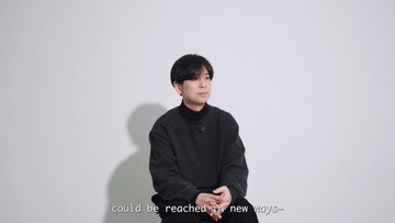 A young man with dark hair wearing a black shirt sits against a plain background, with subtitle text reading 'could be reached by new ways-' at the bottom.