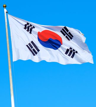 The South Korean flag waves against a clear blue sky, symbolizing the nation's newly established stance on cryptocurrency as a strategic state asset under the proposed "National Asset Basic Act," which would bring Bitcoin under formal government asset management.