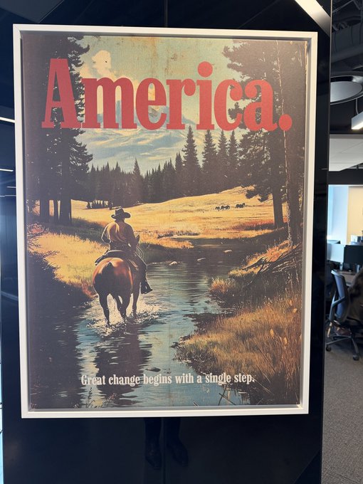 A framed poster on a wall with the text "America." in red at the top, depicting a cowboy on horseback crossing a stream, with "Great change begins with a single step." at the bottom.