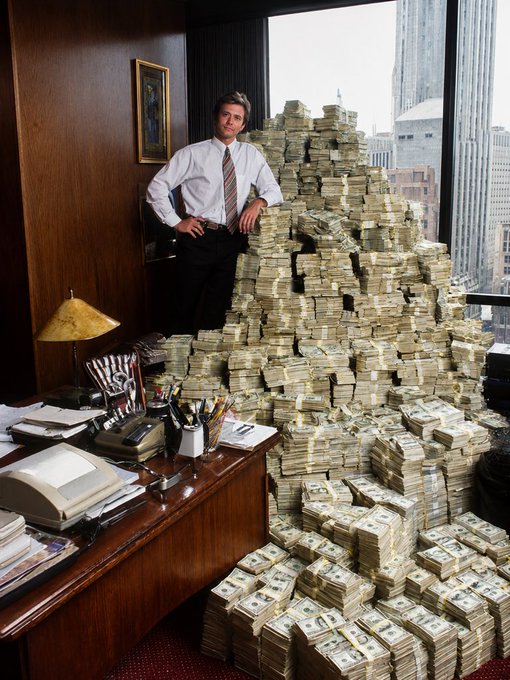 A young businessman in a white shirt and striped tie stands proudly beside a towering mountain of stacked cash bundles in his wood-paneled office, with city skyscrapers visible through the window behind him. The image perfectly embodies the post's theme of holding early, staying patient, and achieving massive parabolic wealth gains through memes.