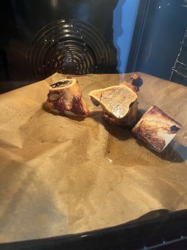 Several pieces of browned, caramelized candy or dessert rest on crumpled parchment paper inside an oven.