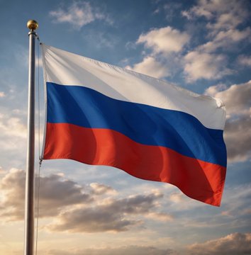 A photograph of the Russian flag (white, blue, and red horizontal stripes) waving on a flagpole against a partly cloudy sky at sunset.