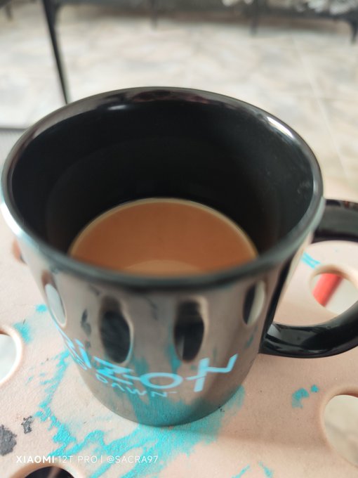 The image features a black mug with a blue logo, sitting on top of a table. The mug appears to be empty or nearly empty, suggesting that someone has recently used it for their morning coffee. The background of the photo shows a tiled floor, indicating an indoor setting like a café or kitchen area. There is also text visible in the image, which reads "Café todos los días #hive". This could be a caption from a social media post or a message related to the café's theme.
