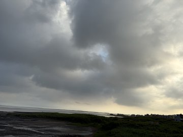 A moody coastal landscape under heavy, overcast gray clouds with a small body of water visible in the distance.